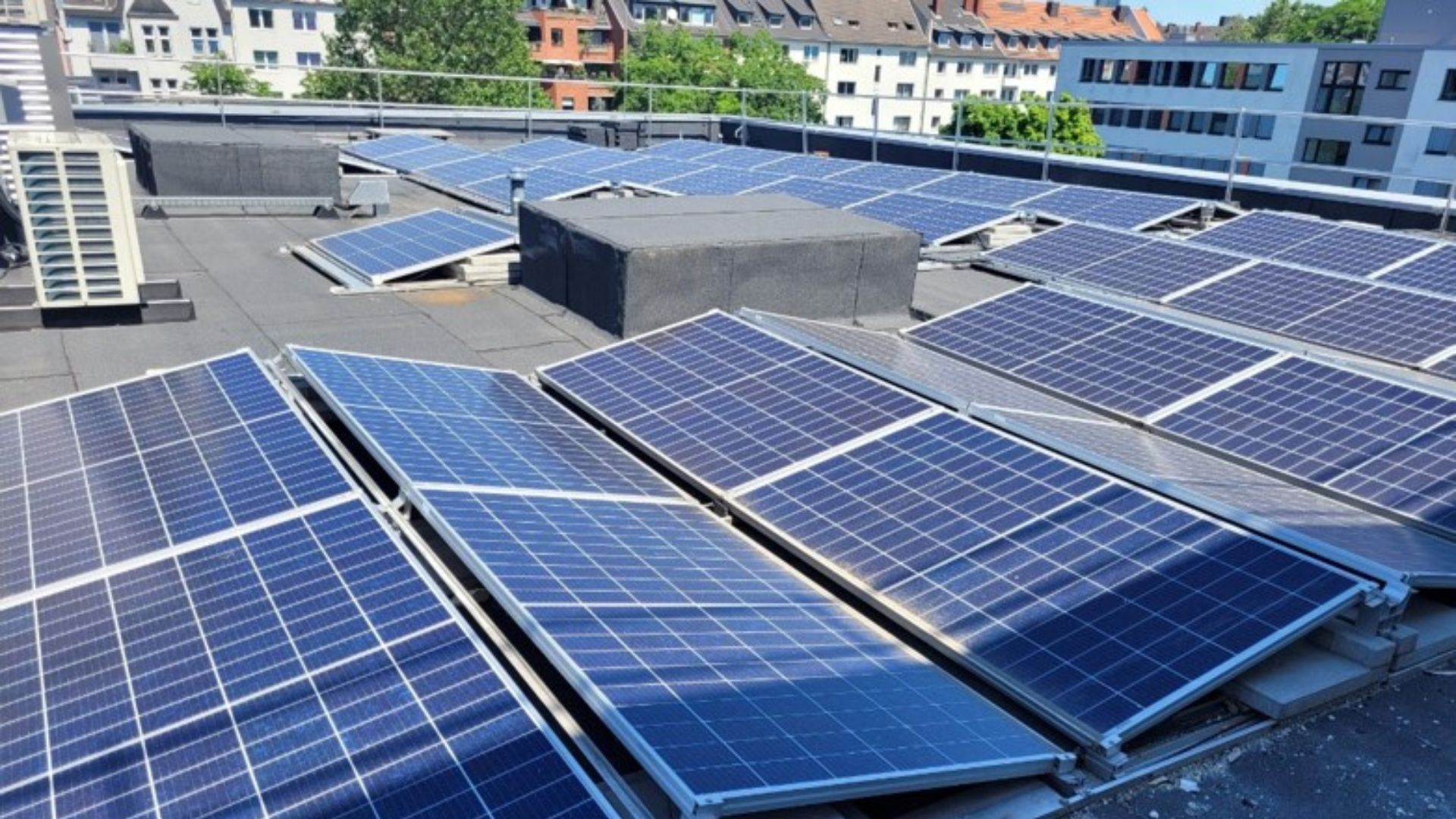 Auf dem Dach eines Krankenhauses ist eine große Photovoltaikanlage aufgebaut, im Hintergrund sieht man die Dächer der benachbarten Häuser.